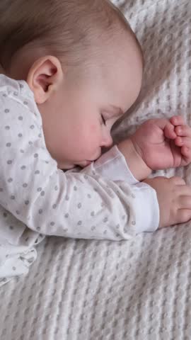 Peaceful little newborn child sleeping soundly on white textured blanket surface. Sweet tiny toddler wearing polka dot pajamas resting in bed during healthy daytime nap at cozy home nursery.