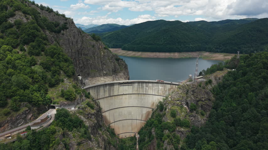 High viewpoint surveys the dam structure, winding access road and surrounding Carpathian valley under cloudy skies.
