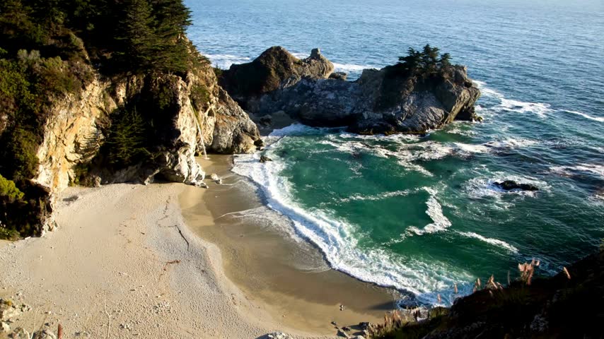 Beautiful coastal cove with turquoise ocean waves crashing on sandy beach cliffs