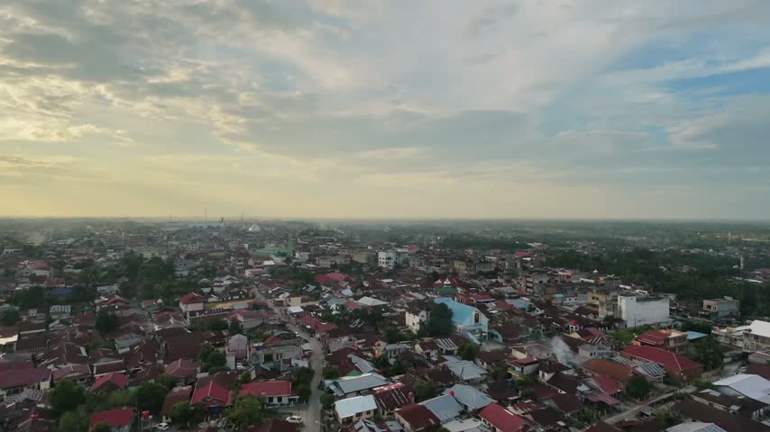 Panoramic aerial perspective of a vast residential townscape with compact houses and winding streets as day turns to night. Sunset sky with clouds, city lights starting to glow