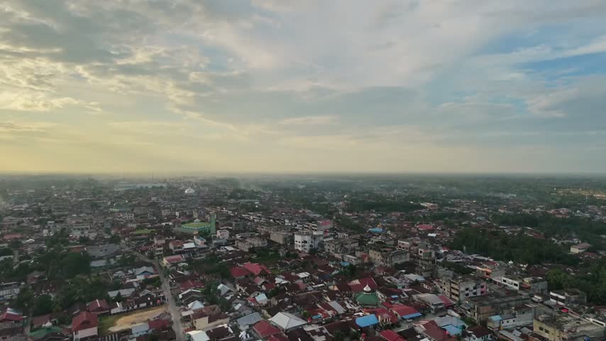 Panoramic aerial perspective of a vast residential townscape with compact houses and winding streets as day turns to night. Sunset sky with clouds, city lights starting to glow