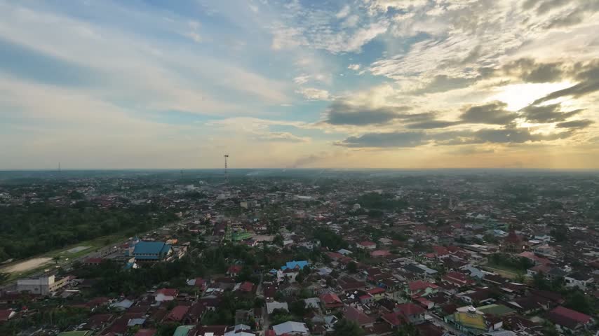 Aerial view of a small town settlement during sunset, with houses and buildings under a dramatic cloudy sky. Urban landscape, evening twilight, and community travel concept.