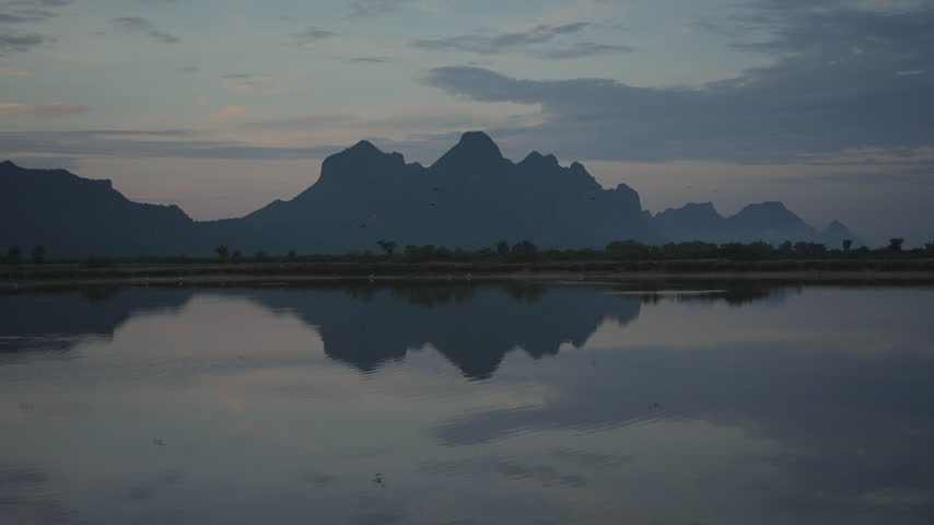 A tranquil view of jagged mountain silhouettes casting a perfect mirror reflection across the still surface of a lake under a soft evening sky