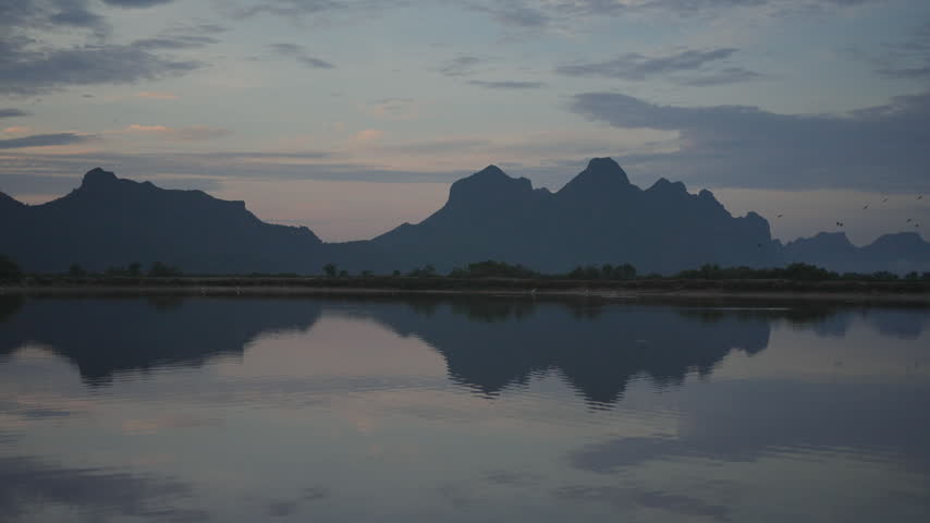 A tranquil view of jagged mountain silhouettes casting a perfect mirror reflection across the still surface of a lake under a soft evening sky
