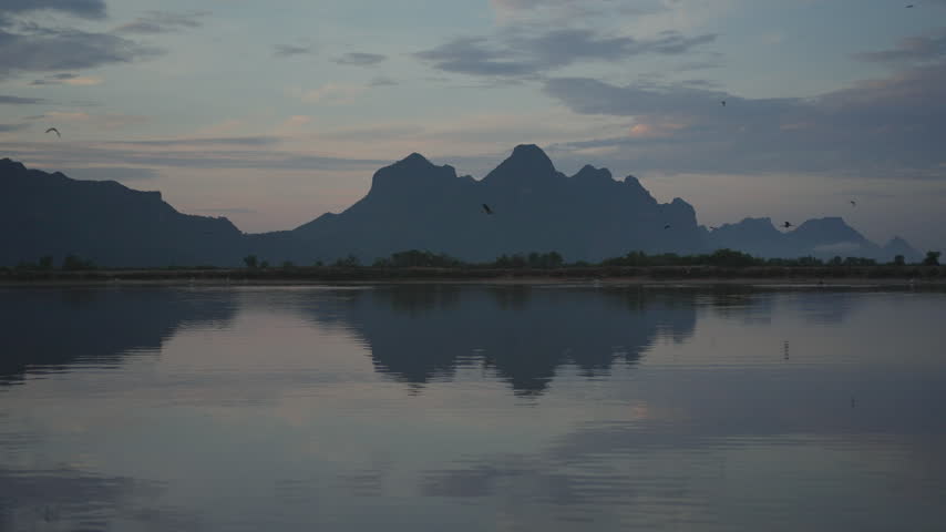 A tranquil view of jagged mountain silhouettes casting a perfect mirror reflection across the still surface of a lake under a soft evening sky