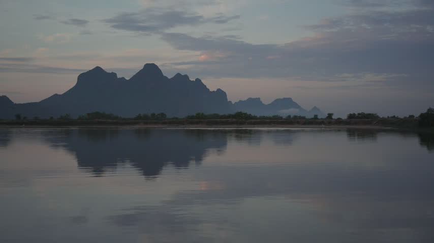 A tranquil view of jagged mountain silhouettes casting a perfect mirror reflection across the still surface of a lake under a soft evening sky