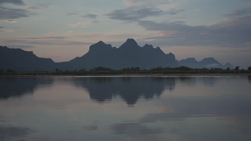 A tranquil view of jagged mountain silhouettes casting a perfect mirror reflection across the still surface of a lake under a soft evening sky