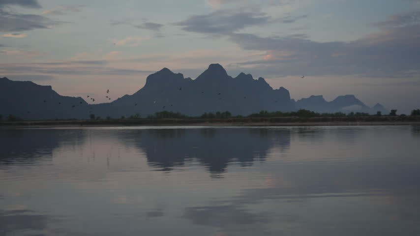 A tranquil view of jagged mountain silhouettes casting a perfect mirror reflection across the still surface of a lake under a soft evening sky