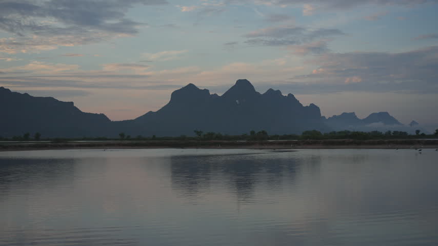 A tranquil view of jagged mountain silhouettes casting a perfect mirror reflection across the still surface of a lake under a soft evening sky