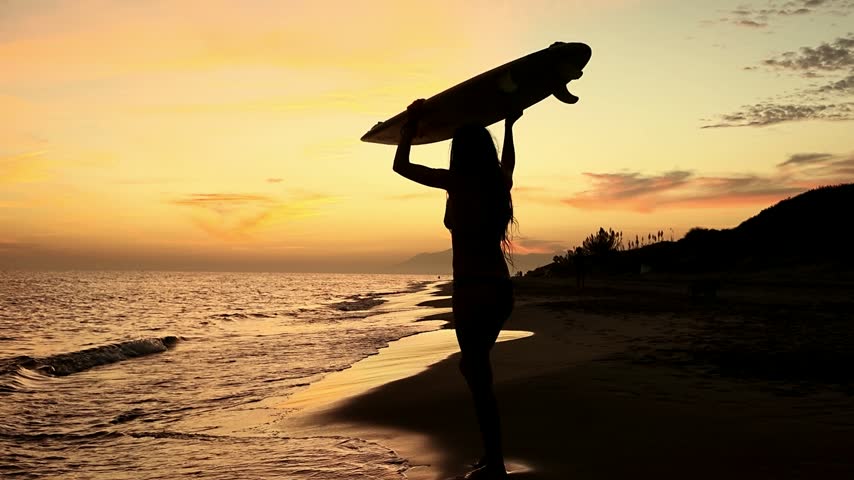 Female surfer carrying a surfboard above her head while running into the ocean at sunset, silhouette against the evening sky, representing surfing action, water sports, active outdoor adventure, summer beach lifestyle, ocean recreation and freedom.