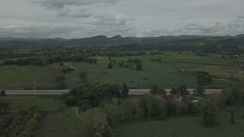 Scenic aerial shot of agricultural fields with trees and distant hills under overcast weather.