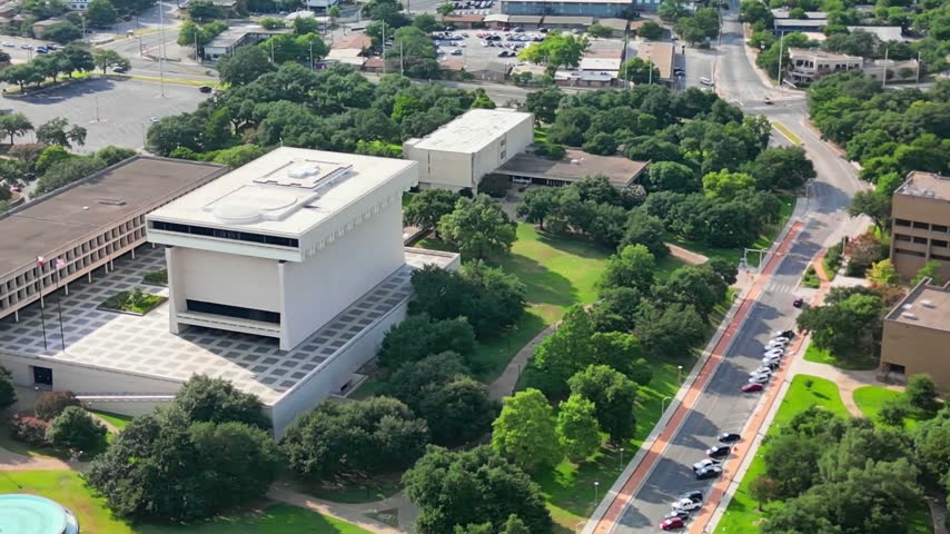 High-angle aerial drone shot overlooking the iconic brutalist architecture of the Lyndon Baines Johnson Presidential Library and Museum located on the University of Texas campus in Austin, Texas, showcasing its massive monolithic stone structure, the open plaza, and surrounding green parklands on a clear day.