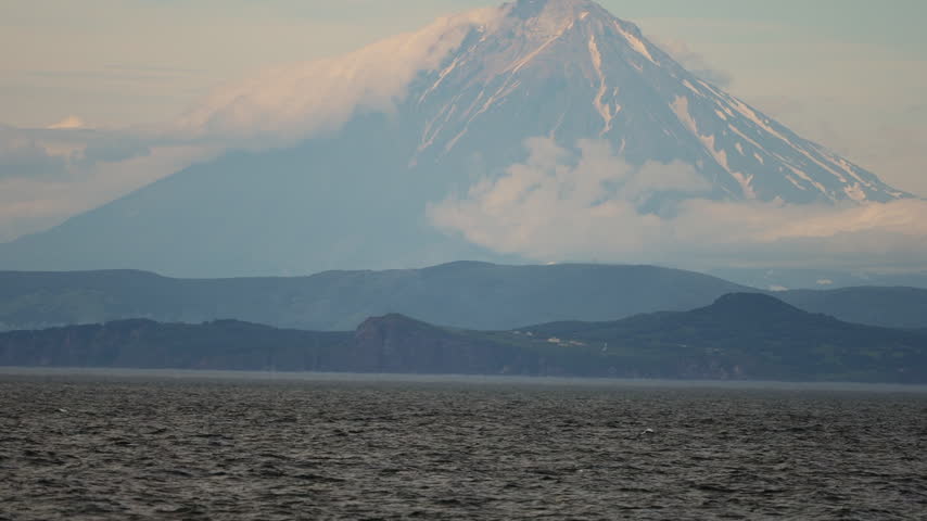 Slow motion of humpback whale breaching out of Pacific Ocean in front of snow-capped volcano, wild Megaptera novaeangliae off coast of Kamchatka, Russian Far East