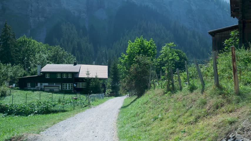 Sunlight and shadow moving across a swiss chalet on a dirt road nestled in a lush green valley. Switzerland