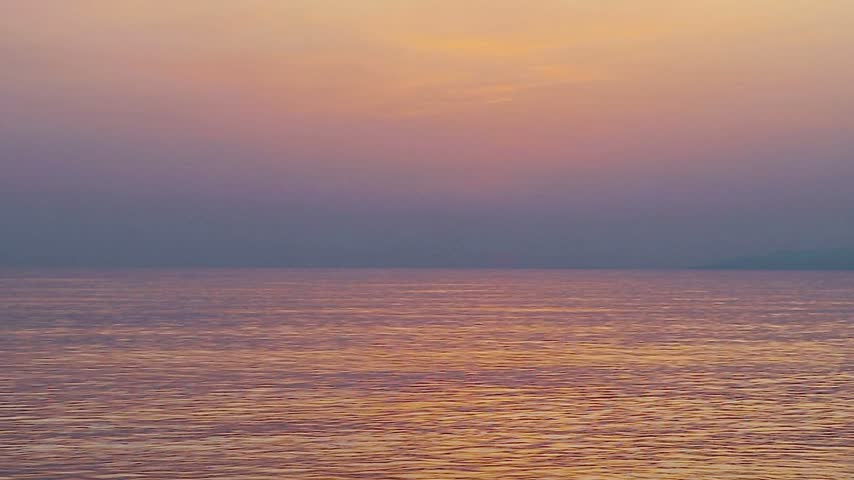 Serene sunset over calm ocean waters casting a warm, glowing twilight reflection across the gentle rippling surface during evening twilight.   