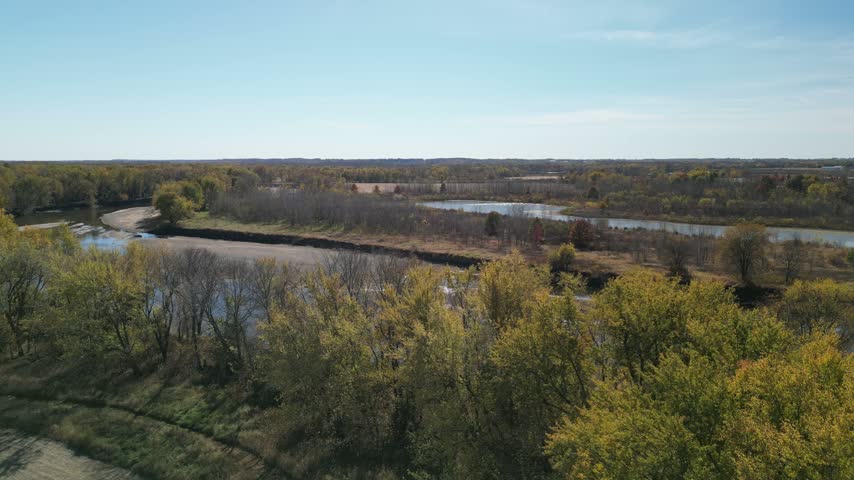 Flying low over fall tree tops covered in changed leaves on a bright summer day to the Iowa River in South Eastern Iowa, the water is very low at a horse shoe bend. On a bright sunny day. 4k, drone