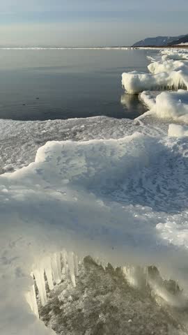 Vertical video of Baikal Lake in December. Waves wash up ice mounds known as Sokui onto beach, shores become covered with whimsical ice crusts and icicles. Unusual waterscape. Changing of seasons