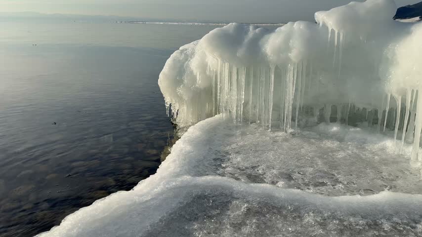 Video of ice-covered shore of Lake Baikal on cold quiet December day. View of coast with white ice floes and icicles during freeze-up period. Scenic waterscape. Changing of seasons. Natural background
