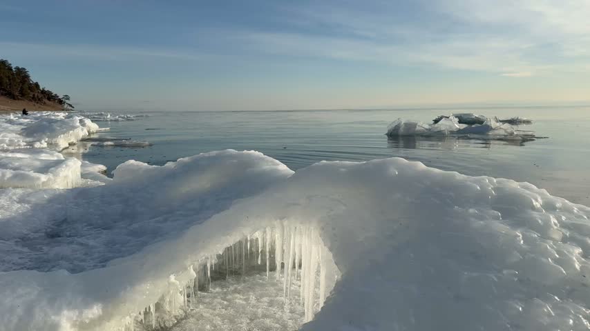 Video of Baikal Lake in morning during December freeze-up. An ice-bound shore set against frosty dawn over blue calm water. Scenic waterscape. Natural backdrop. Travel and outdoor recreation