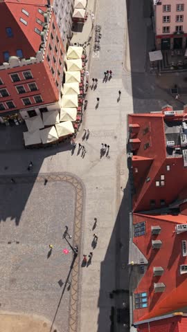 Aerial view of bustling street in Wroclaw, Poland, featuring pedestrians walking, outdoor cafes with umbrellas, and vibrant red-roofed buildings