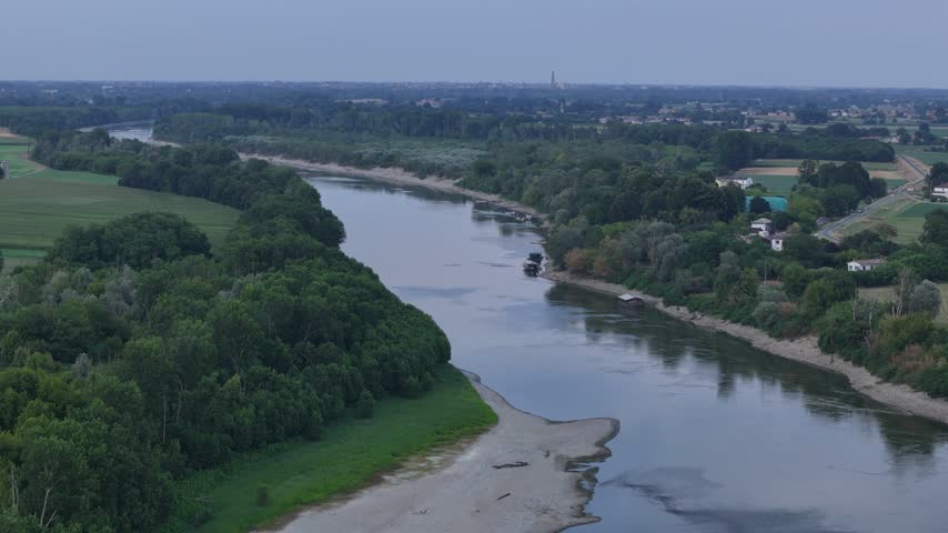 Po River near Isola Serafini flows between riparian woodland, exposed sediment and agricultural fields in the Piacenza area, captured during a drone ascent.