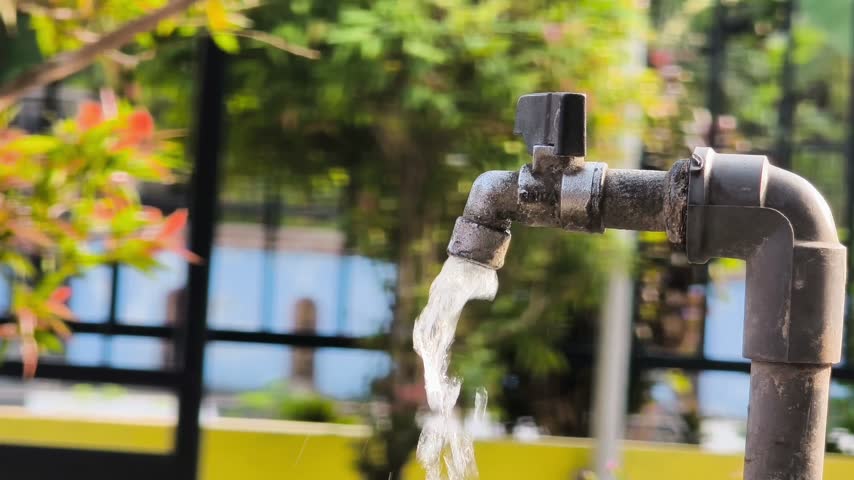A close-up shot showing water flowing from an outdoor garden tap against a blurred background.