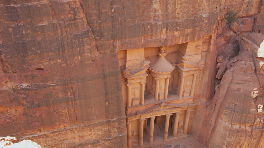 Aerial view of Al-Khazneh, the Treasury of Petra in Jordan, carved into rose sandstone cliffs with monumental Nabataean columns and a narrow canyon setting.