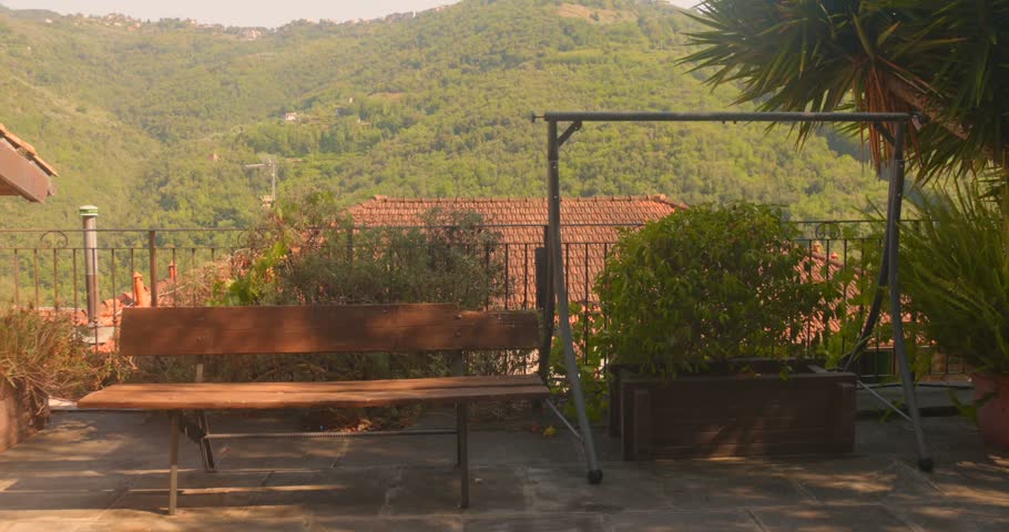Terrace bench overlooking terracotta rooftops and forested hills in Apricale. Warm golden light.