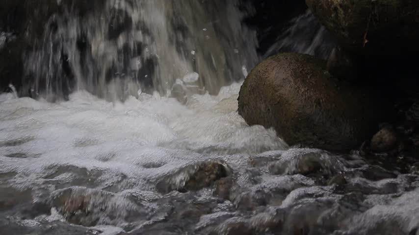A detailed view of a rushing waterfall with white foamy water flowing over textured grey rocks and pebbles, showcasing the raw power of nature.