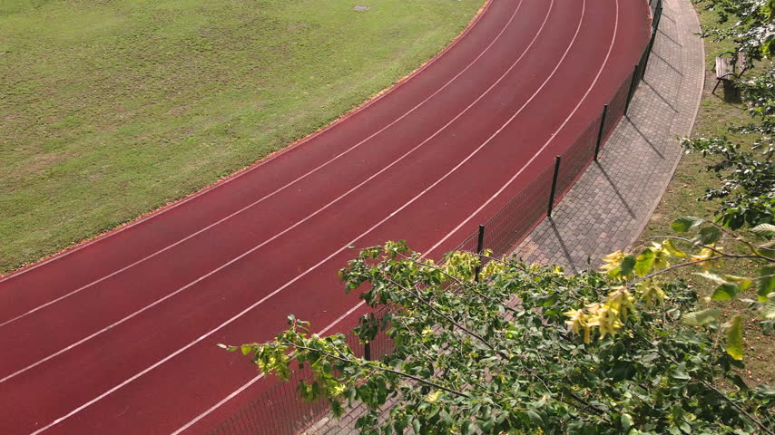 Woman running on stadium track during morning workout. Female athlete jogging along red running lane in sunlight. Fitness, cardio and active lifestyle.