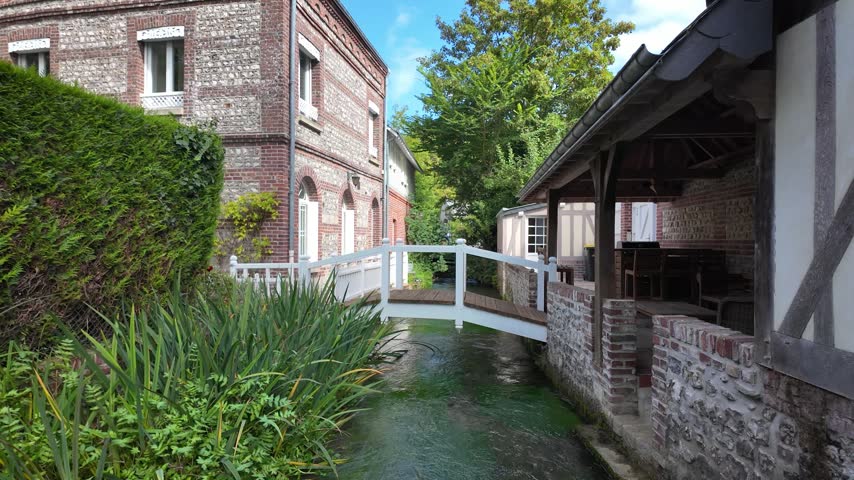 Slow motion footage of a small white footbridge crossing the Veules River between traditional buildings in Veules-les-Roses, Normandy, France