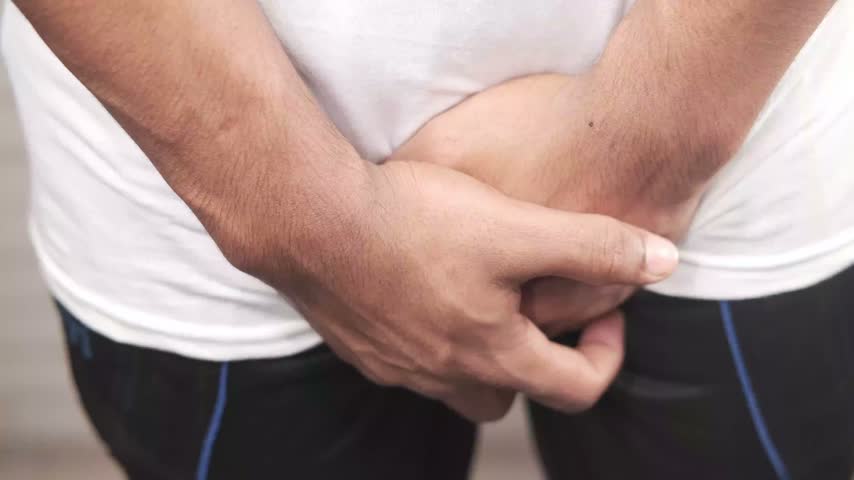 Person experiencing urinary urgency or bladder pain holding their private parts with hands demonstrating discomfort or need to visit restroom in outdoor setting close up shot.