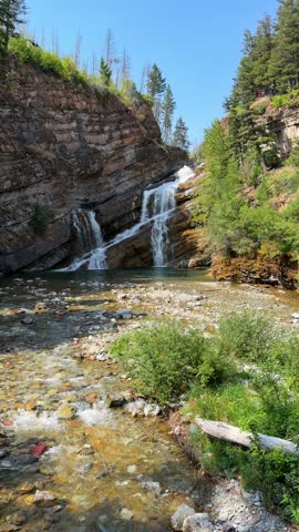 Cameron Falls cascading over layered rock cliffs into a green pool at Waterton Lakes National Park in Alberta, a scenic waterfall surrounded by trees in summer.