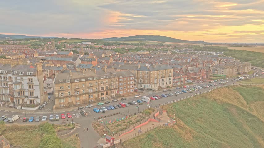 Saltburn-by-the-Sea rises inland from Marine Parade, with Victorian terraces, Valley Gardens and the Cleveland Hills visible beyond the town, Redcar and Cleveland, England, drone ascent.