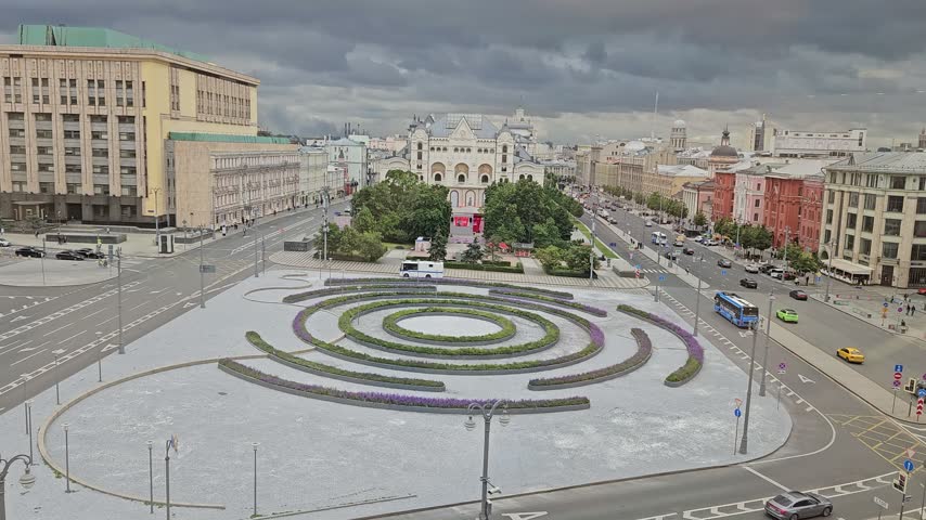 Circular green pattern dominates the city Lubianskaya Square. Cars move along wide, paved roads nearby. Sky is overcast with dark clouds above in Moscow, Russia