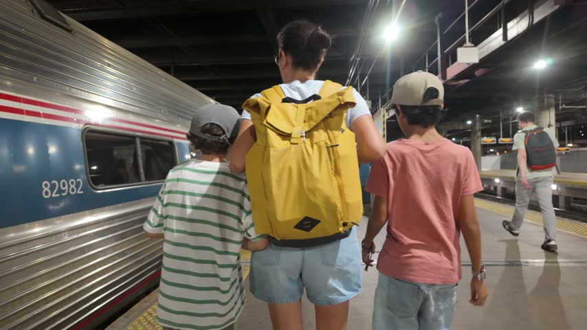 Young family, a mother with her two sons, enjoying a vacation as they walk along a railway platform at night, ready for an exciting journey by train to their next destination