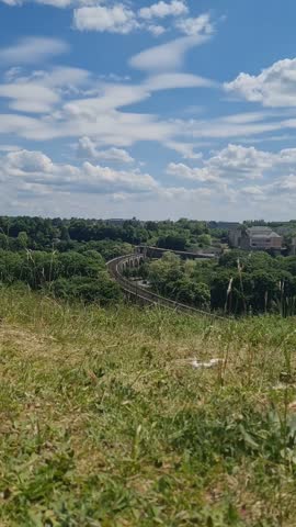 Train crosses a distant aqueduct bridge in Luxembourg with grass filling the foreground of a hilltop.