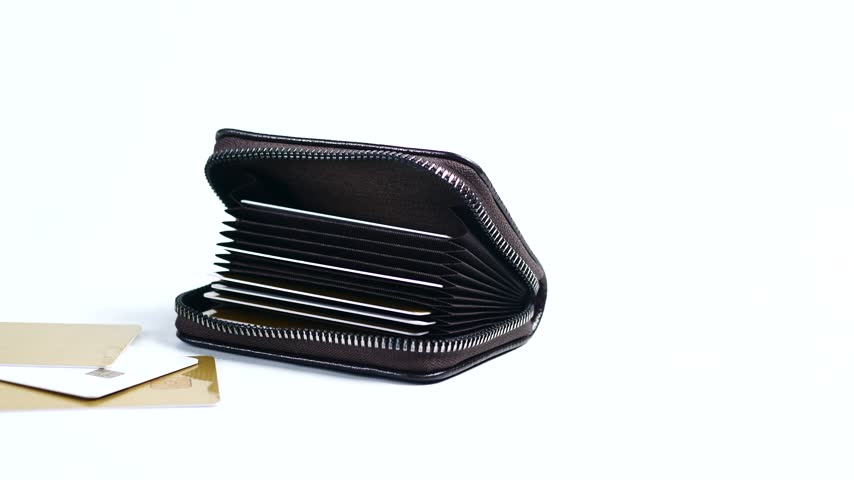 Close up shot of dark brown leather card holder featuring many slots for credit cards standing on white studio background with two additional bank cards laying beside it.