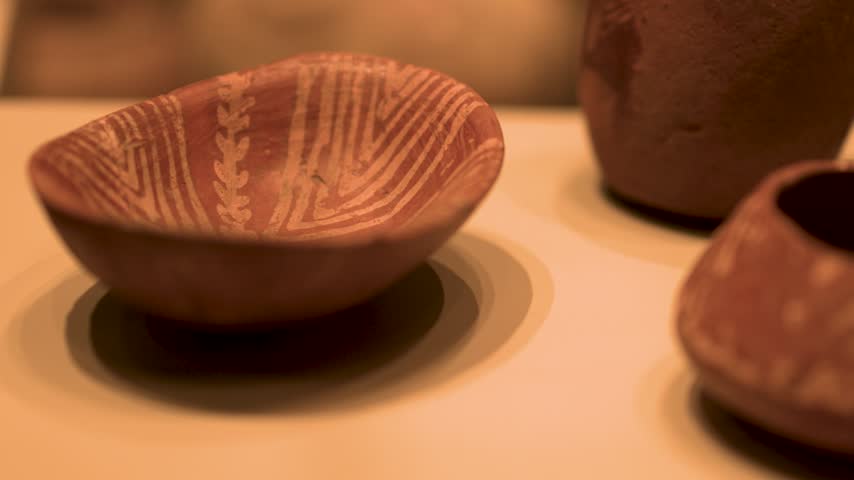 Close-up of an ancient decorated terracotta ceramic bowl exhibited in a museum showcase.