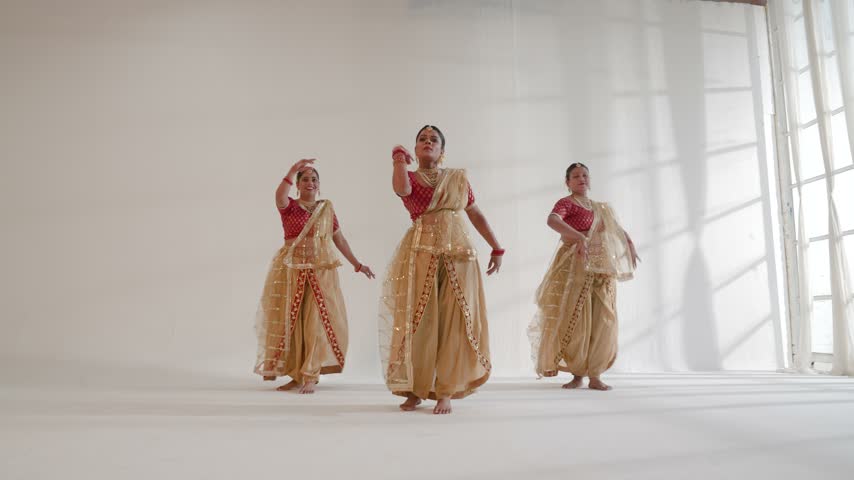 Three women performing a traditional dance routine inside a studio