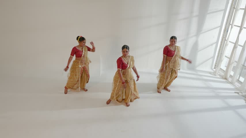 Three women performing a traditional Indian dance in a bright studio