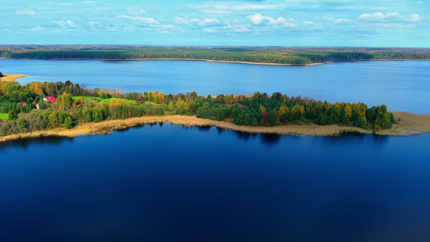 Aerial view of vibrant autumn foliage surrounding tranquil lake waters under partly cloudy skies
