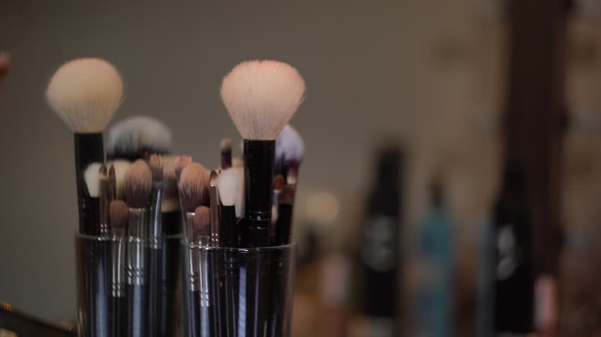 Hands of makeup artist selecting the right brush from a collection of professional cosmetic tools in beauty salon, preparing for makeup session.