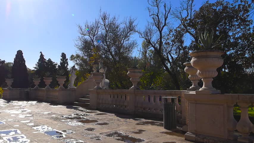 Stunning outdoor view of the historic gardens at the National Palace of Queluz in Portugal, with puddles on the stone terrace reflecting the bright sun and blue sky after a recent rain