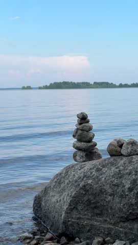 A rocky lakeshore featuring large stones stacked in the shape of a tower. This video is suitable for posts about travel and outdoor recreation.