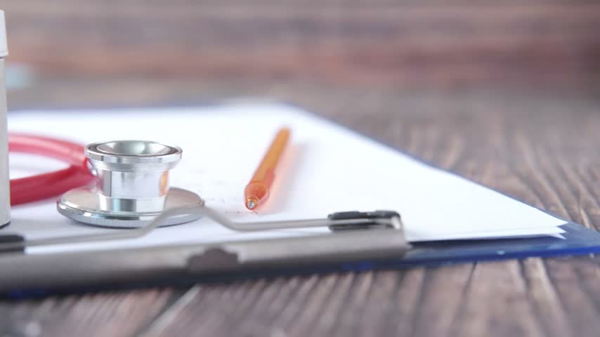 Essential medical equipment displayed on wooden table featuring stethoscope pill bottle and patient chart ready for clinical assessment or healthcare professional consultation.