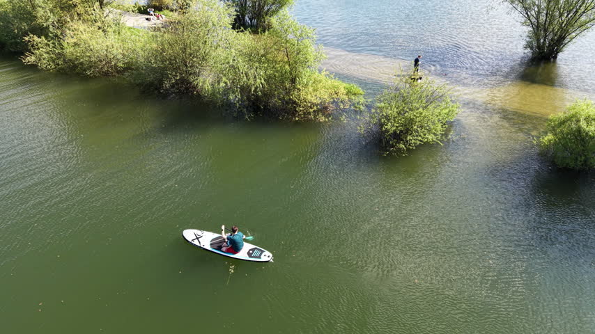 Overhead drone view of a small boat moving near trees on a green lake.