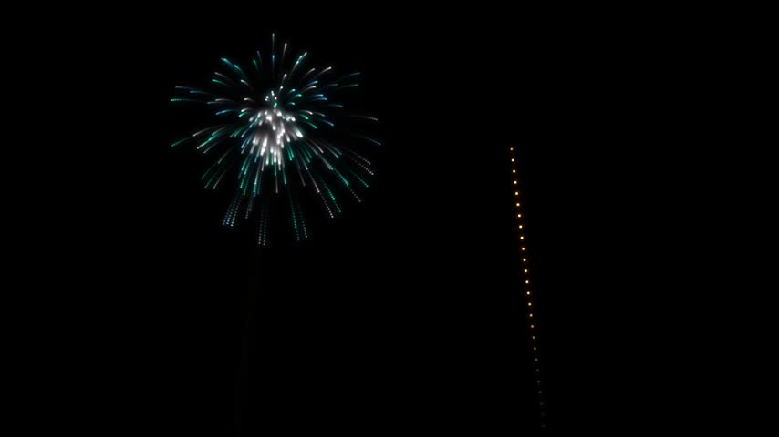 A vibrant blue and white firework burst in the night sky next to a vertical string of glowing orange lights