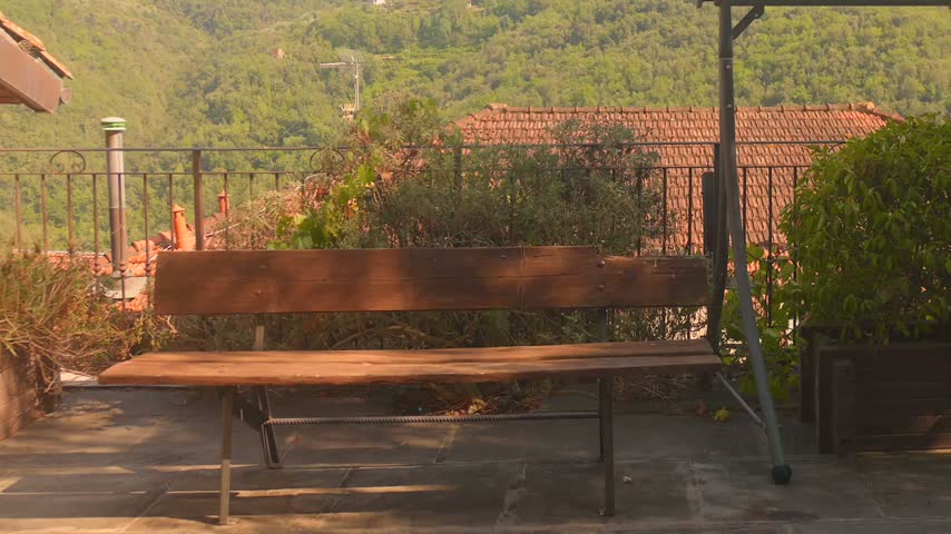 Terrace bench overlooking terracotta rooftops and forested hills in Apricale. Warm golden light.