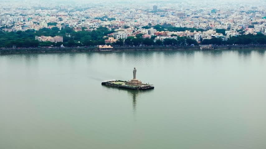 Hussain Sagar lake with Gibraltar Rock Gautama Buddha Statue, Residential buildings and floodgates at hyderabad, telangana, india. day time, arc shot, drone shot, 4k.
